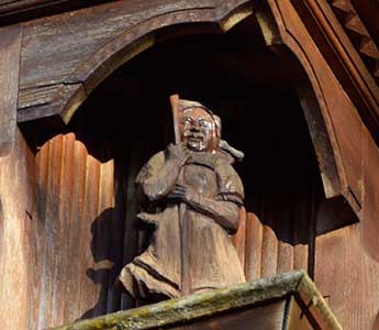 Balkon mit reich geschnitzten Figuren an einem Bauernhof in Grünenbach - Detail Frau mit Sense