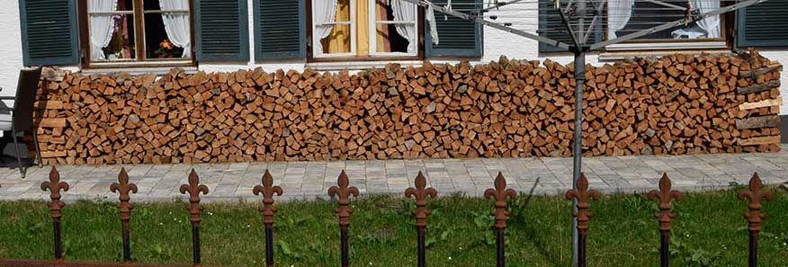 Ein eiserner Zaun um den Garten - mit Brennholz vor der Hütte in der Holzstaplergemeinde Trauchgau