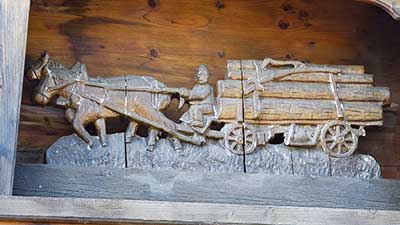 Balkon mit reich geschnitzten Figuren an einem Bauernhof in Ussenburg - Detail Holzfuhrwerk