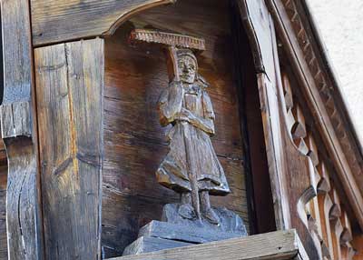 Balkon mit reich geschnitzten Figuren an einem Bauernhof in Ussenburg - Detail Frau mit Heurechen